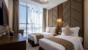 Habitación de hotel con dos camas, un escritorio, un televisor y un amplio ventanal con cortinas.