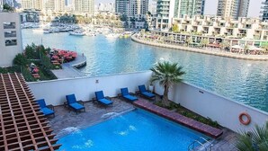 A rooftop pool with blue lounge chairs, a view of a marina with boats, and high-rise buildings in the background. - Three Bedroom Apartment In Marina By E R (Dubai)