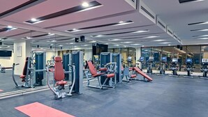 Une salle de sport équipée de divers appareils d’exercice, de miroirs et d’un tapis rouge sur le sol.