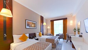Une chambre d’hôtel avec deux lits, un bureau, une chaise et une grande fenêtre avec des rideaux.