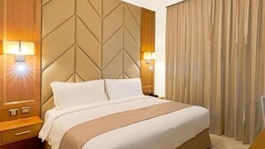A hotel room with a large bed, wooden headboard, two bedside lamps, and a large window with curtains. - One Bedroom Apartment Near Fujairah Mall (Fujairah)