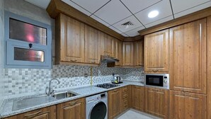 A kitchen with wooden cabinets, a washing machine, a microwave, and a tiled backsplash. - One Bedroom Apartment Near Fujairah Mall (Fujairah)