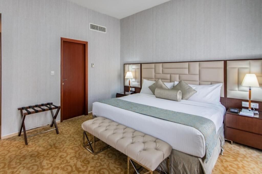 A hotel room with a large bed, a bench, a nightstand, and a door.