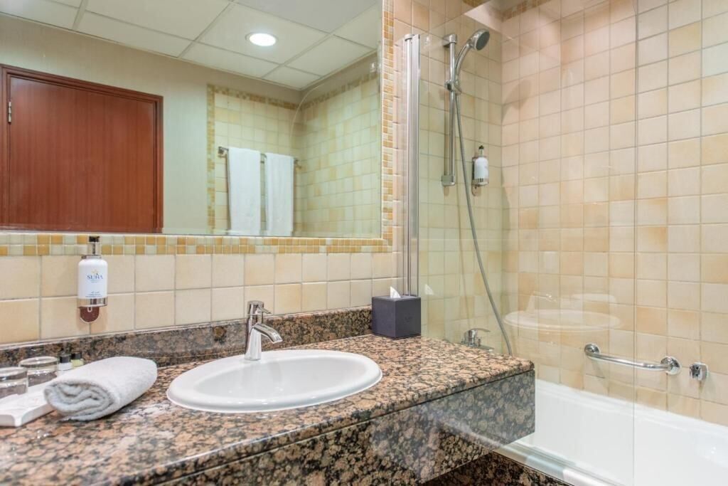 Ein Badezimmer mit Granitplatte, Waschbecken in Weiß, einem Spiegel, einer Dusche und einem Handtuchhalter.