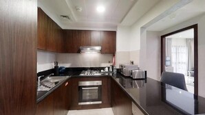 A modern kitchen with wooden cabinets, stainless steel appliances, and a black countertop. - One Bedroom Apartment In Jaddaf By E R (Dubai)