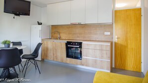 Eine kompakte Küche mit Einbauofen, Essbereich mit Stühlen und einem flachbildfernseher, der über der Arbeitsfläche angebracht ist.