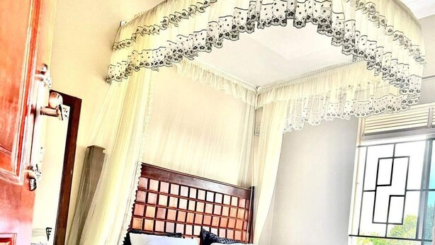 A four-poster canopy bed with a wooden headboard, white bedding, and a patterned rug. - Apartment - Sleeps 2 - Parking - Garden (Kampala)