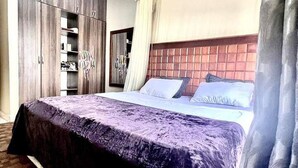 A hotel room with a large bed, a wardrobe, and a mirror. - Apartment - Sleeps 2 - Parking - Garden (Kampala)