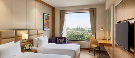 Habitación de hotel con dos camas, un escritorio, un televisor y vistas a la ciudad.