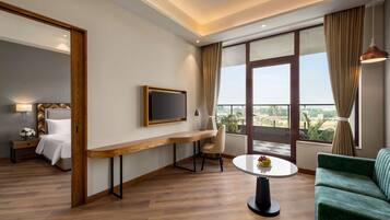Habitación de hotel con cama, escritorio, televisión, sofá y balcón con vistas.