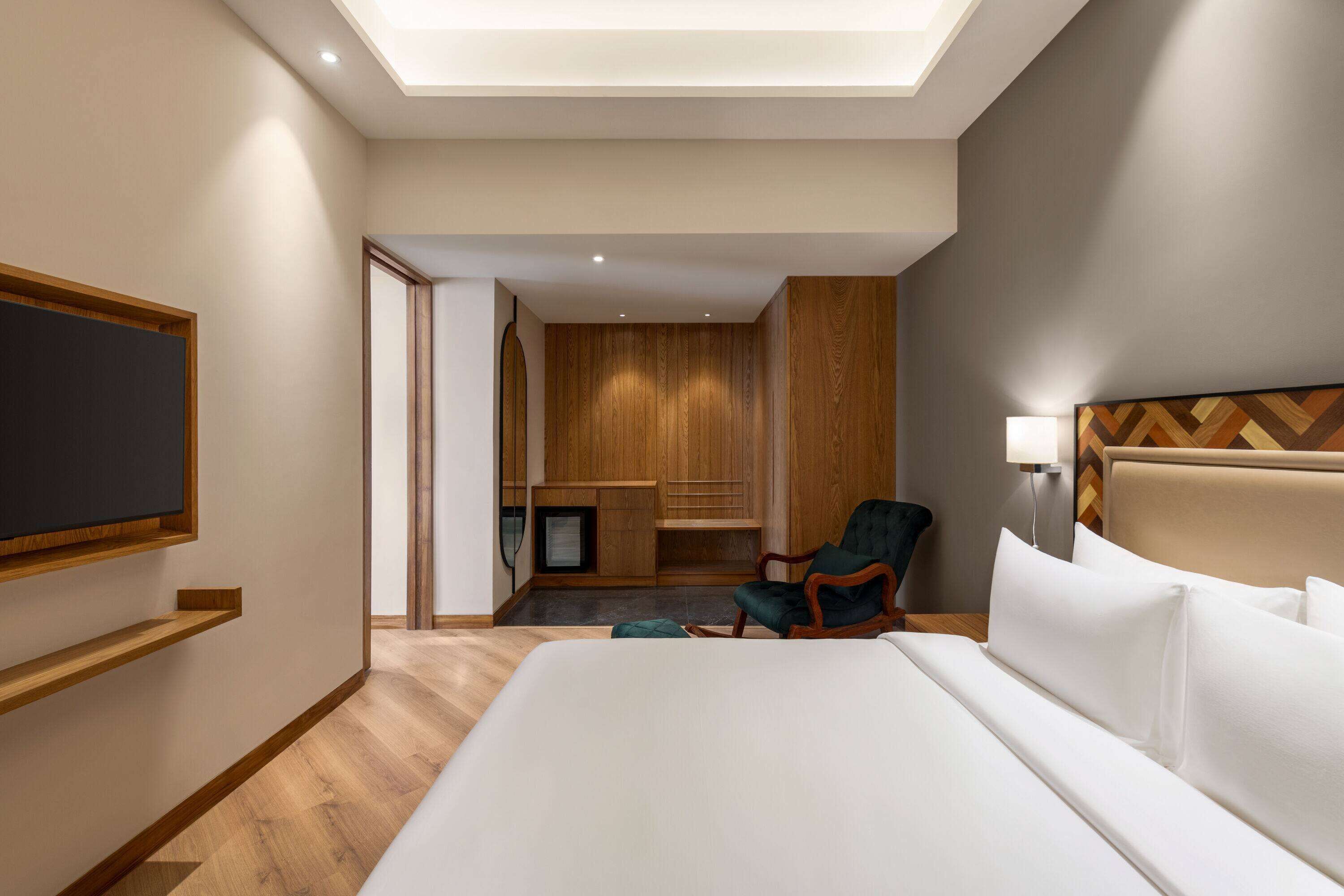 Una habitación de hotel con una cama grande, un televisor montado en la pared, un armario de madera, un escritorio y una silla.
