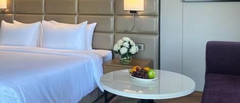 Una habitación de hotel con una cama, una mesa redonda con fruta, una silla morada y un cuadro en la pared.