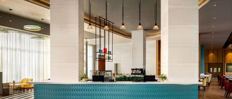 A modern hotel lobby with a reception desk, seating area, and a staircase.