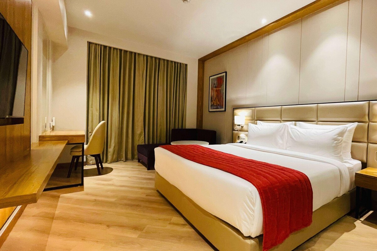 A hotel room with a bed, a desk, a chair, a TV, and a window with curtains.
