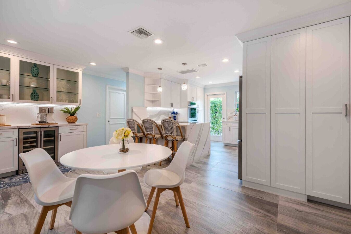A modern kitchen with white cabinetry, a dining area with a round table and chairs, and a large wardrobe.
