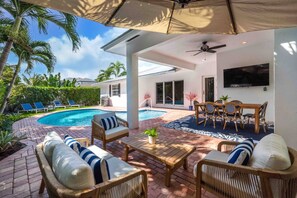 Uma área externa coberta com piscina, cadeiras de descanso e uma mesa de jantar.