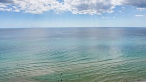 A wide view of a beach with clear water and a distant horizon under a partly cloudy sky. - Balcony & Beach Access: Oceanfront PCB Condo (Panama City)