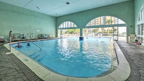 An indoor swimming pool with clear water, a tiled floor, and a view of the outside through large arched windows. - Balcony & Beach Access: Oceanfront PCB Condo (Panama City)