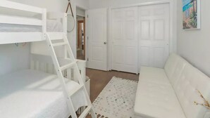 A room with a bunk bed, a white sofa, a patterned rug, and a door with a painting. - La Casita Solar II (Clearwater)