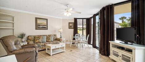 A living room with a sofa, a recliner, a coffee table, a TV on a cabinet, and a dining area with chairs and a table.