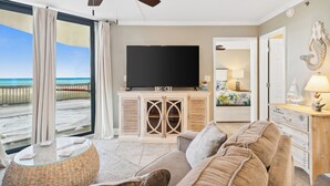 A living room with a television, a sofa, and a view of the beach. - Sunbird Beach Resort by Book That Condo (Panama City Beach)
