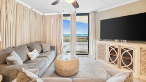 A living room with a sofa, a round coffee table, a television, and a view of the beach. - Sunbird Beach Resort by Book That Condo (Panama City Beach)