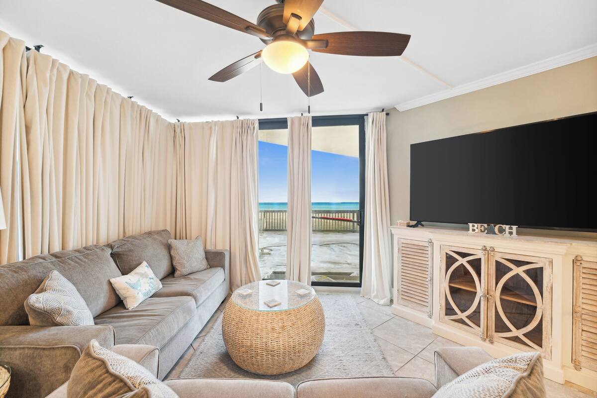 Ein Wohnzimmer mit einer Couch, einem runden Couchtisch, einem Fernseher und Blick auf den Strand.