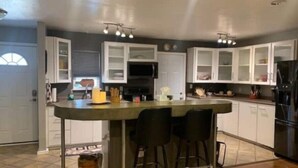A kitchen with a central island, bar stools, white cabinets, and a black refrigerator. - Cozy 3bd. 2bth home, Panoramic views, near UNR, DT, FRWY & RENO AIRPORT. (Reno)