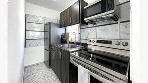 Una cocina moderna con armarios oscuros, un refrigerador de acero inoxidable, un microondas, una estufa y un horno.
