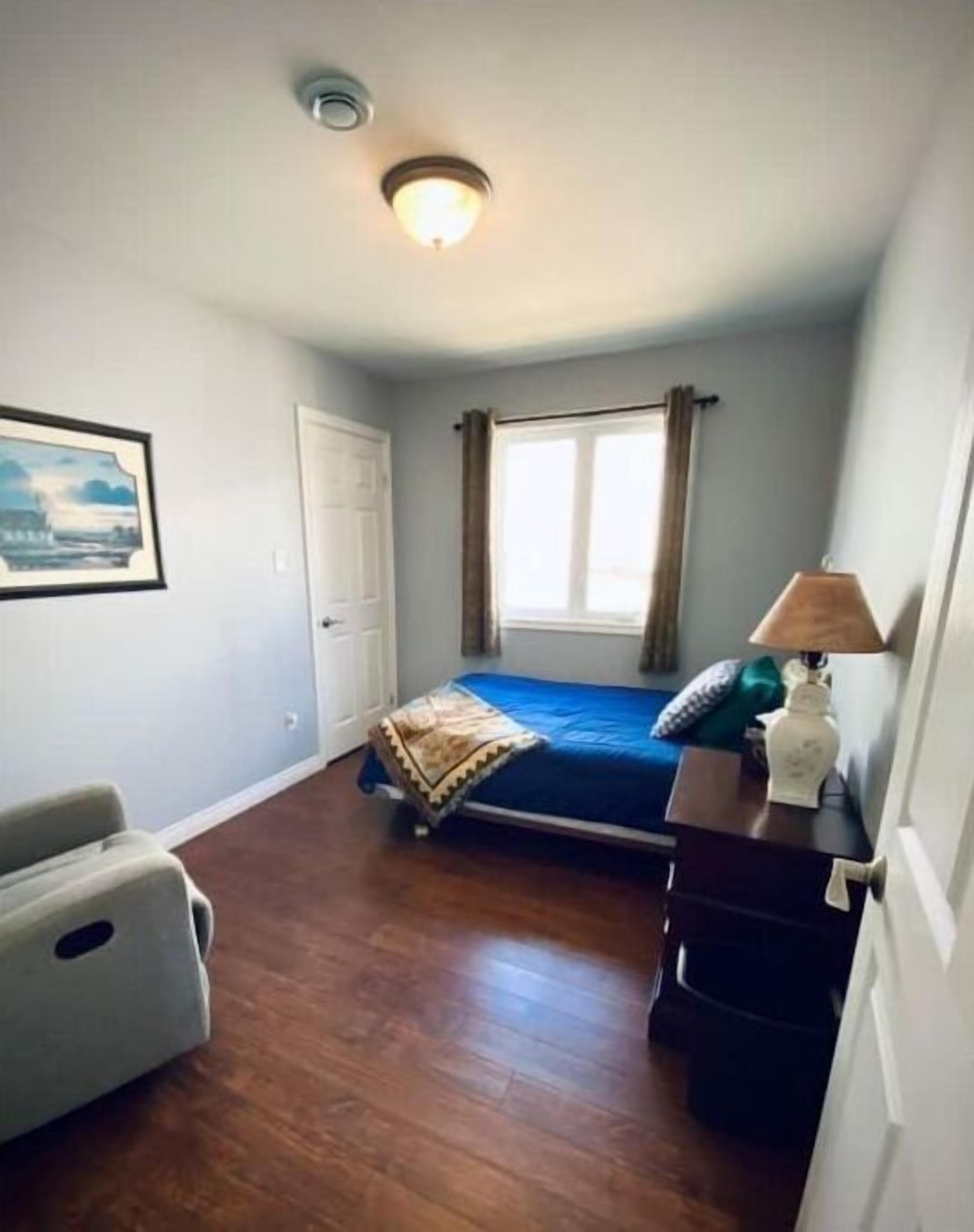 Une chambre à coucher comprenant un lit, un bureau, une chaise, une fenêtre avec des rideaux et un luminaire au plafond.