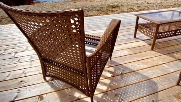 A wooden deck with two wicker chairs and a table, overlooking a body of water and a forested landscape.