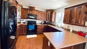 A kitchen with wooden cabinets, a black refrigerator, a stove, and a sink.