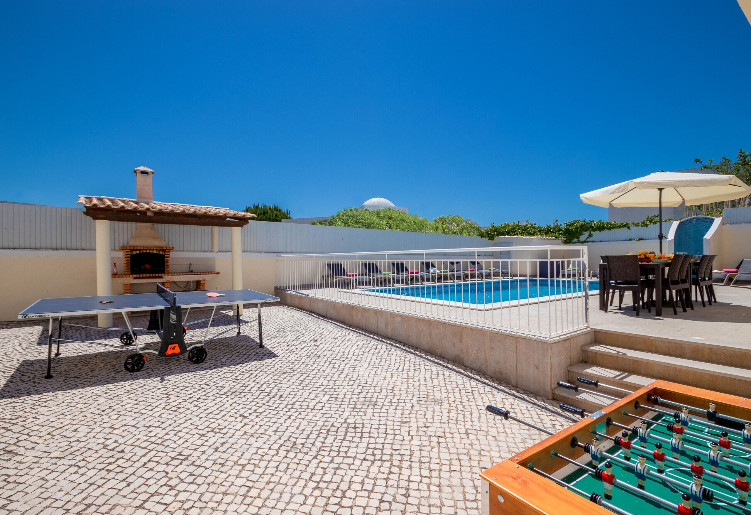 A poolside area with a foosball table, a barbecue grill, and a table with chairs.