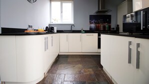 A modern kitchen with white cabinets, a black countertop, and a large window providing natural light. - Carlton Grove by Tŷ SA (Newport)
