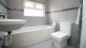 A bathroom with a bathtub, toilet, sink, and a window with a decorative tile border. - Carlton Grove by Tŷ SA (Newport)