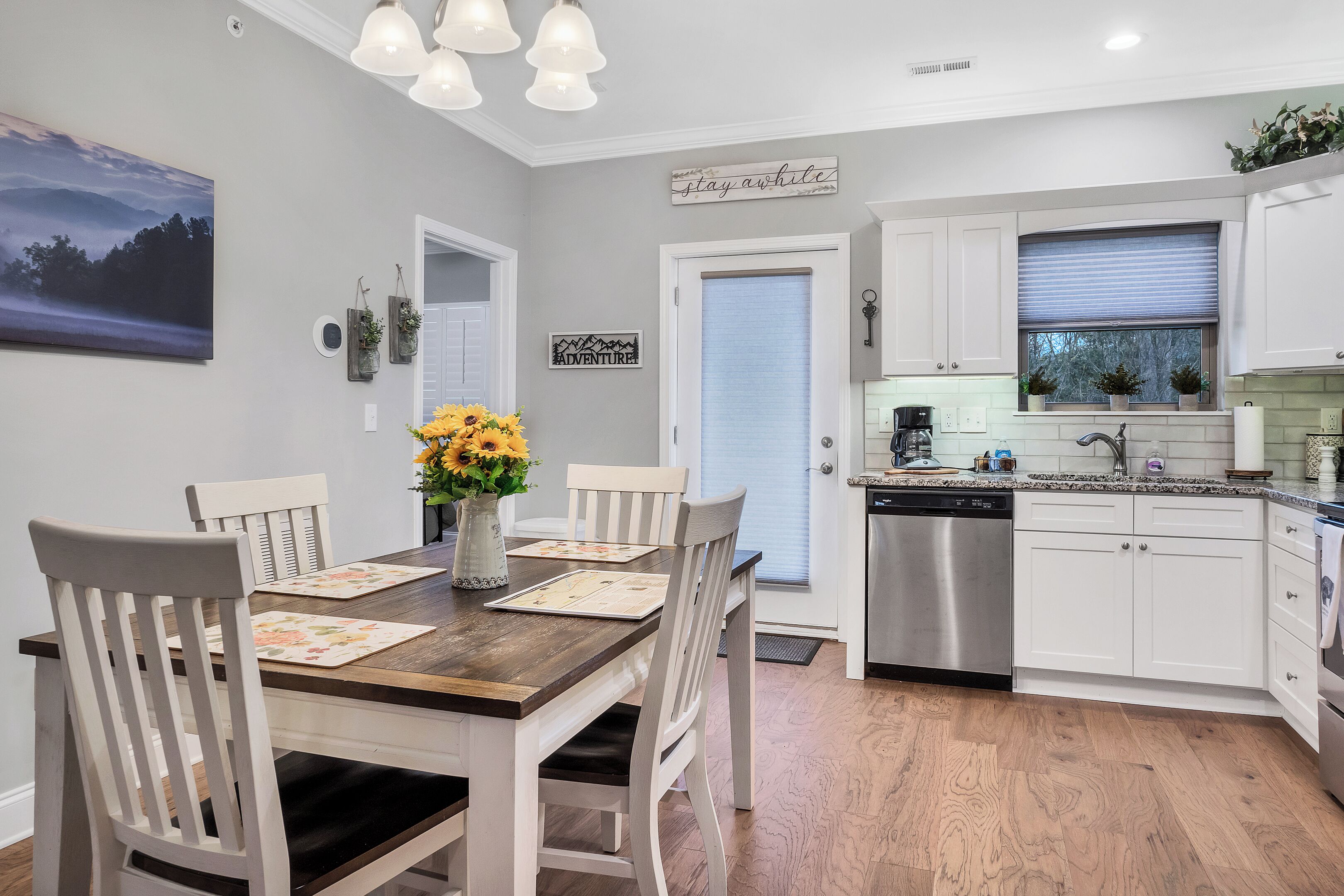 A kitchen with white cabinets, a wooden dining table, and a vase with sunflowers.