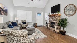 A living room with a fireplace, a ceiling fan, and a television mounted on the wall.