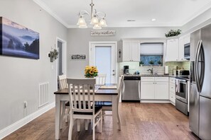 Una cocina moderna con armarios blancos, electrodomésticos de acero inoxidable y un comedor con mesa y sillas de madera.