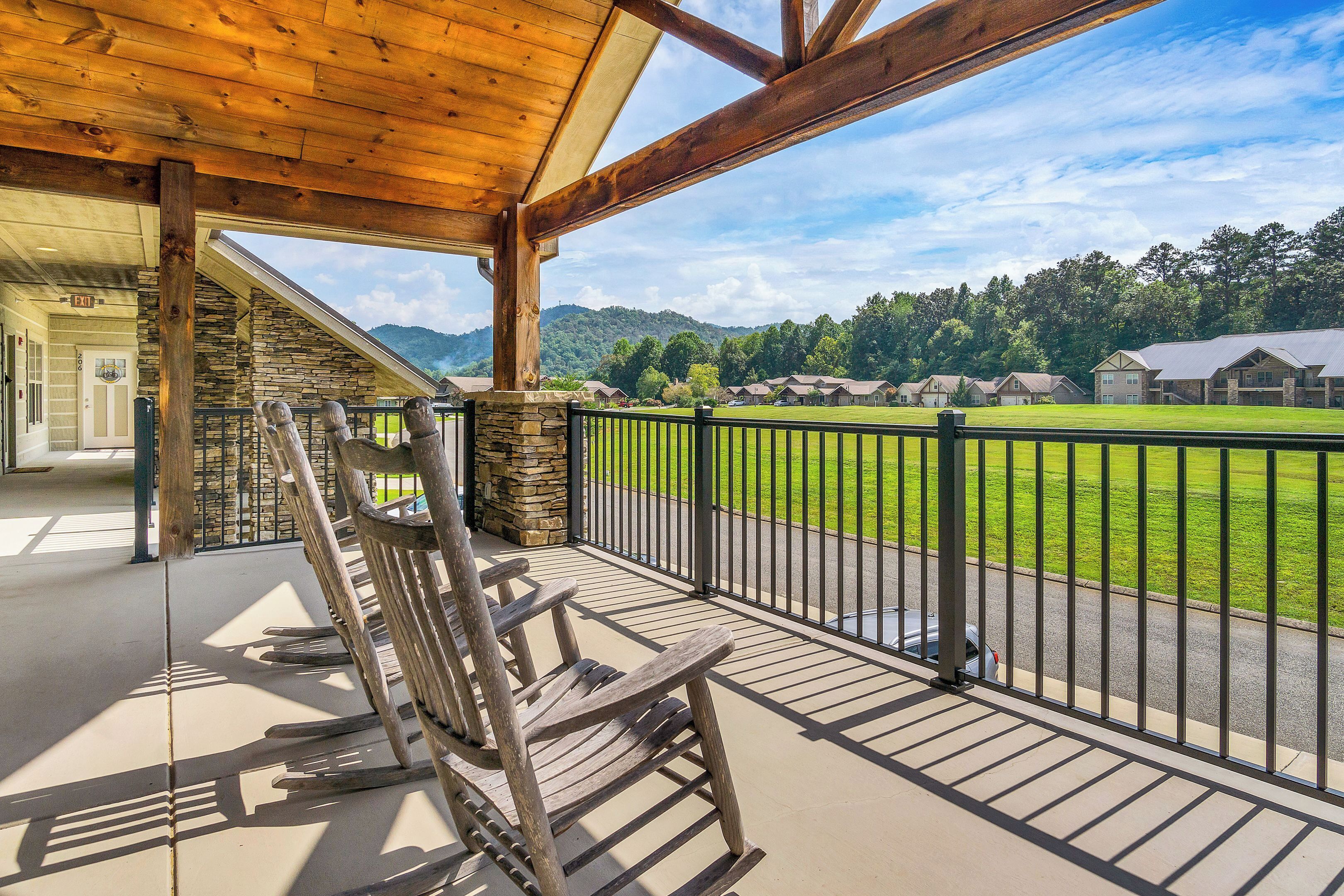 A covered porch with a wooden rocking chair, stone walls, and a view of a green field and houses in the distance.
