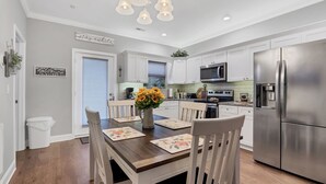 A modern kitchen with white cabinetry, stainless steel appliances, and a dining area with wooden chairs and floral placemats.