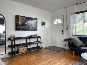 A modern living room with a wooden floor, a black entertainment unit, a TV displaying 'PUP ACADEMY', and a black sofa with a cushion.