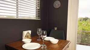 A dining table set with white plates, bowls, and cutlery, a clock on the wall, and a window with blinds.