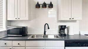 Een moderne keuken met witte kastjes, een roestvrijstalen spoelbak, een magnetron, een koffiezetapparaat en drie hanglampen.