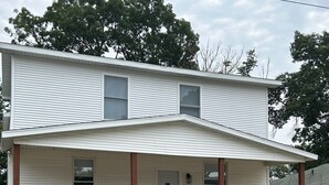 A two-story house with a front porch, a small front yard with a gravel pathway, and a staircase leading to the porch. - Lakeside on Greenwood (Muskegon)