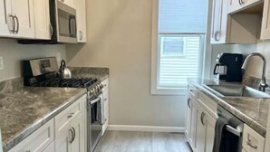 A kitchen with white cabinets, a microwave, a stove, and a window with blinds. - Lakeside on Greenwood (Muskegon)