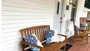 A wooden bench and chair set on a wooden deck with white siding walls. - Lakeside on Greenwood (Muskegon)