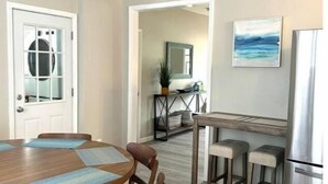 A dining area with a wooden table and chairs, a kitchen with a refrigerator, and a view of the outdoors. - Lakeside on Greenwood (Muskegon)
