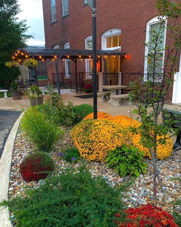 A courtyard with a brick building, outdoor seating, and a variety of plants and flowers.