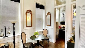 A room with a dining table, chairs, a lamp, and a rug. There are windows with blinds and a door leading to another room.