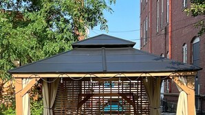 A covered outdoor seating area with wicker furniture and a table, surrounded by potted plants. - Skyline View Penthouse Apartment (Mansfield)